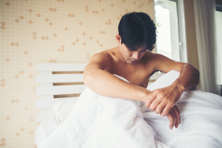 Worried man sitting on bed in the morning, serious thinking something