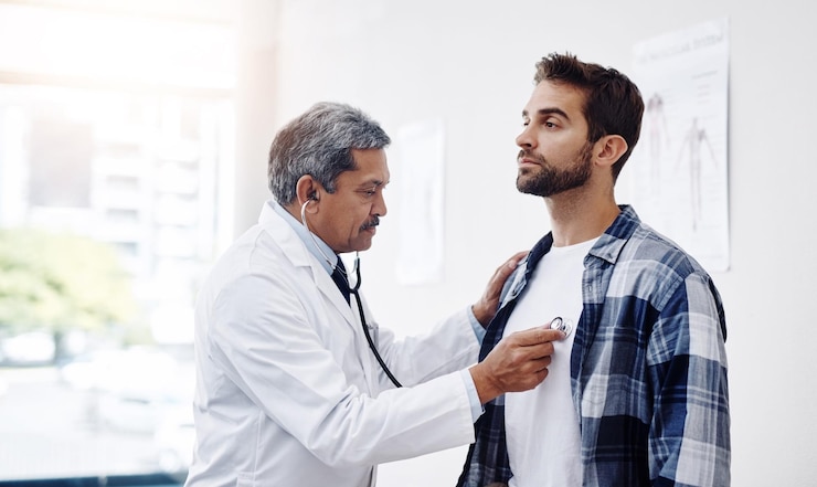 Healthcare patient and doctor with stethoscope for checkup help and wellness at hospital Medicine health care and heart expert with Indian man in doctors office consulting medical professional