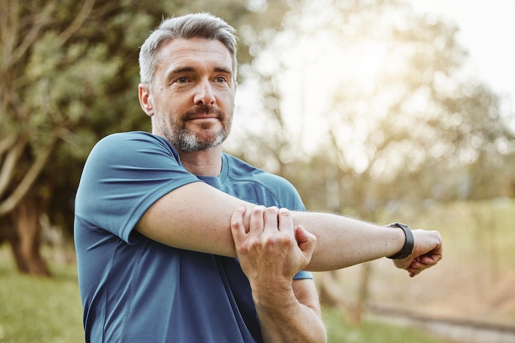 Mature man arm stretching and outdoor for fitness wellness and exercise in a park for health Morning athlete and training in nature with workout and sports of a calm person ready to start run