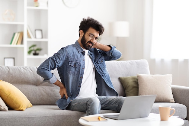 Indian man suffering backache and neckache after working with laptop at home