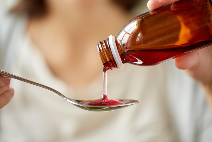 healthcare, people and medicine concept - woman pouring medication or antipyretic syrup from bottle to spoon